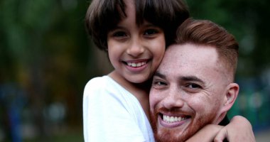 Ebeveyn ve çocuk kucaklaşır ve kucaklaşır. Baba ve genç çocuk farklı etnik çeşitlilikte sevgi ve özen, otantik