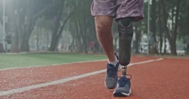 Determined disabled athlete walking forward with prosthetic leg equipment at running track