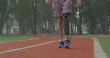 Athletic amputee with prosthetic leg walking forward at running track. Disabled athlete with prosthetic equipment walk forward