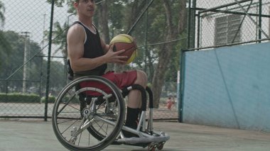 Dışarıda top oynayan engelli bir basketbolcu. Tekerlekli sandalyedeki belden aşağısı felçli kişiye yakın çekim. Spor ve sakatlık kavramı