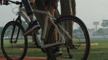 Protez bacaklı engelli bir adam dışarıda bisiklet sürüyor.