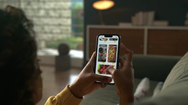 Çevrimiçi Dağıtım menü telefonunu kullanan kişi. Online mağazadaki kadın siparişleri teslimat uygulamasında akıllı telefon kullanıyor. Oturma odasındaki kanepede uzanan kadın.