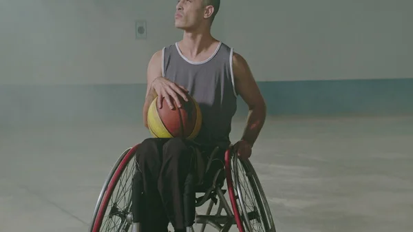 One hispanic disabled basketball player athlete on wheelchair holding ball. Portrait of a latin paraplegic sportive person with disability. Sport and determination concept