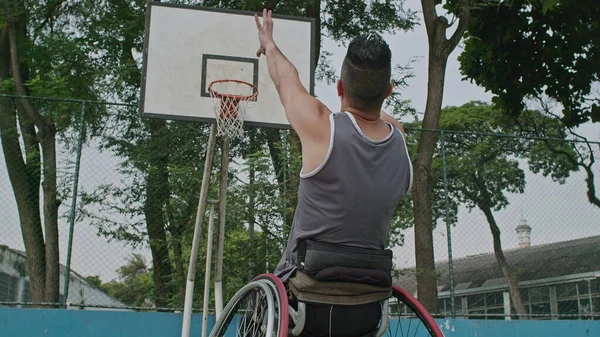 A disabled athlete on wheelchair training basketball. A paraplegic person throwing ball inside hoop and having success on the second trial. Sport disability and determination concept.