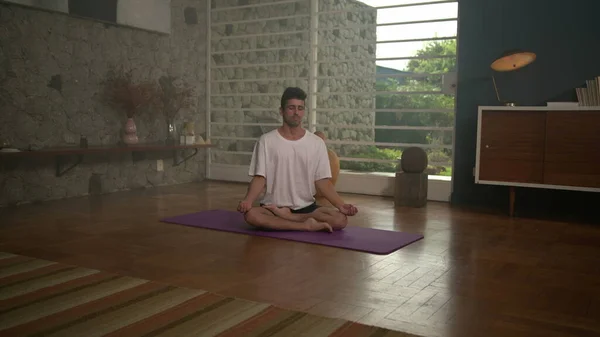 One calm person meditating at home after workout sitting on living room floor inside modern home