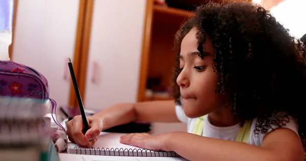 Black schoolgirl studying at home. Female kid doing homework writing notes