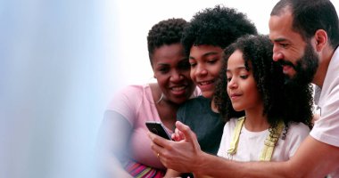 Aile birlikte cep telefonuna bakıyor. Ebeveynler ve çocuklar akıllı telefonun etrafında toplandı
