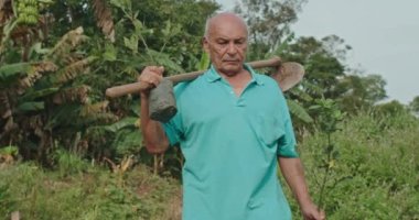 Bir kıdemli adam elinde iki tane fidan saksısı taşıyarak çiftlikte yürüyor ve ağaç dikmeye gidiyor. Kırsal kesimden daha yaşlı, otantik biri.