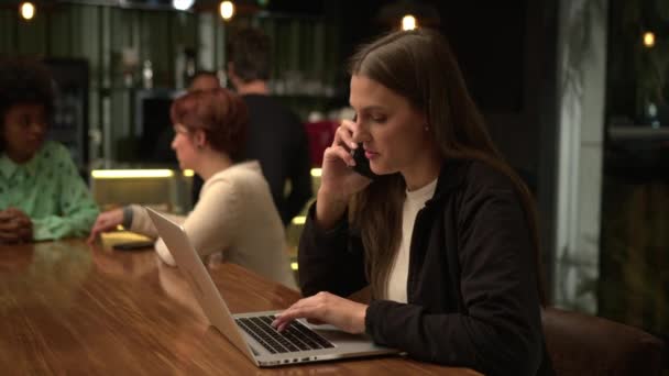 Молодая Женщина Работающая Кофейне Разговаривая Телефону Используя Ноутбук Многозадачность Люди — стоковое видео