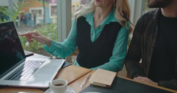 Женщина Исполнительница Объясняет Работу Молодому Работнику Мужчине Перед Ноутбуком Кафе — стоковое видео