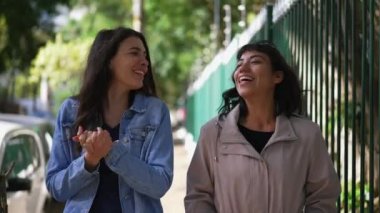Two happy women smiling and laughing while walking in city. Girls real life laugh and smile