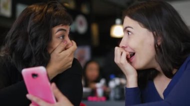 İki genç kadın ShoCK ve SURPRISE ile çevrimiçi olarak akıllı telefon aygıtı kullanarak tepki veriyor. Sosyal medyada UNBELIEF ile kız arkadaşların duygusal tepkisi