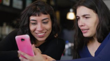 Restoranda takılan cep telefonu ekranını işaret eden iki kadın. Akıllı telefon cihazına bakan kız arkadaşlar içeriği çevrimiçi izliyor