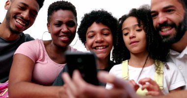 Mutlu melez aile telefon cihazına bakıp gülüyor ve gülümsüyor.