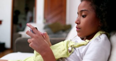 Evdeki koltukta akıllı telefon kullanan küçük siyah kız. Afrika etnik kökeni