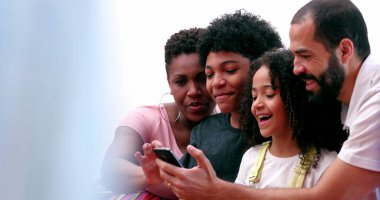 Irklar arası aileler ve etnik çeşitlilikte çocuklar cep telefonuyla sosyal medyaya gülüyorlar.