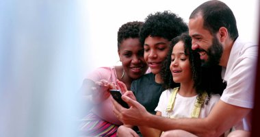 Irklar arası aileler ve etnik çeşitlilikte çocuklar cep telefonuyla sosyal medyaya gülüyorlar.