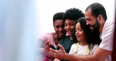 Irklar arası aileler ve etnik çeşitlilikte çocuklar cep telefonuyla sosyal medyaya gülüyorlar.