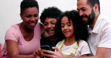 Cep telefonu kullanan ırklar arası bir aile. Akıllı telefon cihazına bakan karışık ırk ebeveynleri ve çocuklar