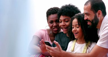 Karışık ırk ailesi ve çocuklar cep telefonu içeriğiyle birlikte gülüyorlar.