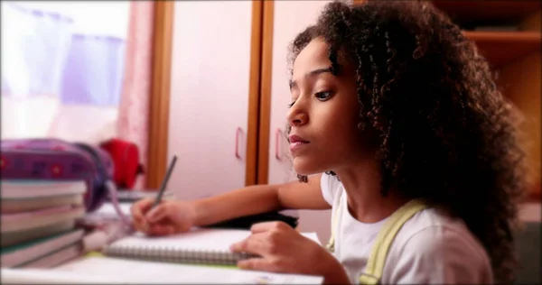 Little school girl studying at home writing notes. Black mixed race ethnicity child homework