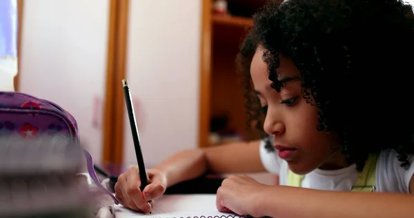 Little girl studying at home, mixed race child writing notes doing homework