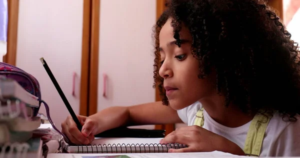 Little girl studying at home, mixed race child writing notes doing homework