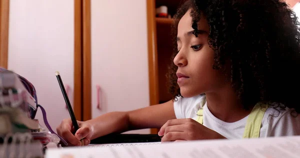 Little girl studying at home, mixed race child writing notes doing homework