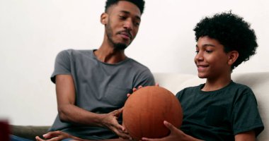 Büyük kardeş küçük kardeşine parmak ile basketbol oynamayı öğretiyor. İki kardeş kaynaşıyor.