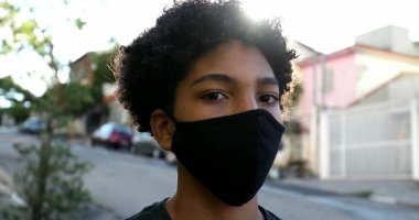 Kentsel sokakta Covid-19 maskeli melez bir genç.