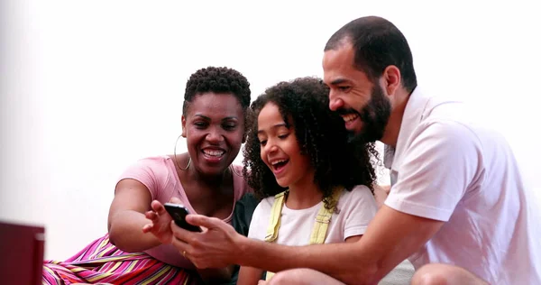 Multi-ethnic family using cellphone. Interracial parents and mixed race children looking at smartphone screen together