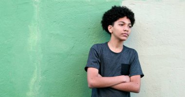 Dışarıda kollarını kavuşturup izleyen genç bir çocuk. Melez zenci çocuk gülümsüyor.