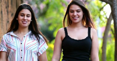 Kız arkadaşlar kaldırımda yürüyüp sohbet ediyorlar.