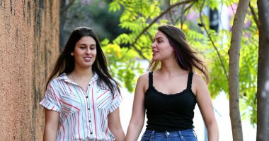 Kız arkadaşlar kaldırımda yürüyüp sohbet ediyorlar.