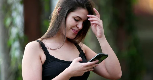 Young millennial woman using smartphone, girl smiling while looking at cellphone screen