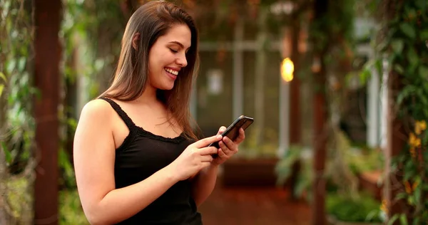 Young millennial woman smiling and laughing while holding smartphone device