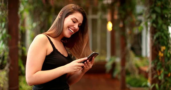 Young millennial woman smiling and laughing while holding smartphone device