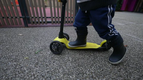 Child legs riding toy scooter outside wearing boots