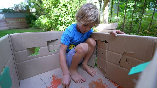 Artistic child painting outside in home garden. Artistic child playing with paint outside in garden painting cardboard box