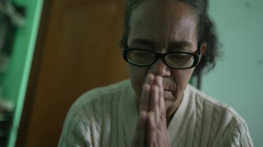 Religious older person praying at home. One hispanic senior woman prays to God