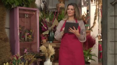 Küçük bir çiçekçi dükkanının sahibi olan bayan girişimci elinde tablet ile online siparişleri kontrol ediyor