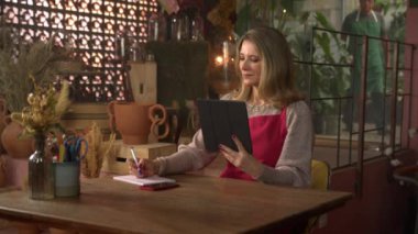 Kadın çiçekçi, elinde tabletle internetten sipariş alıyor. Küçük iş kadını girişimci.