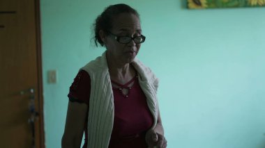 A hispanic senior woman arriving home entering kitchen with groceries