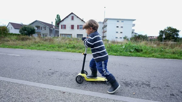 Child rides toy scooter outside