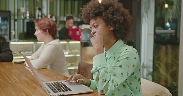 A happy black woman using laptop at coffee shop. One African American girl typing on computer keyboard smiling. A female entrepreneur person looking at laptop screen