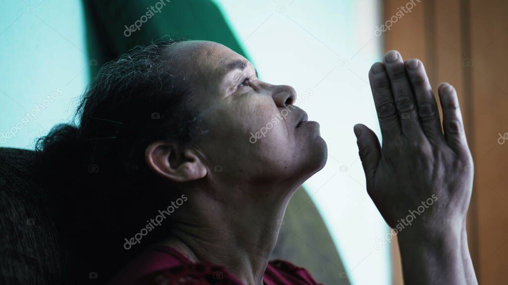 Contemplative South American senior woman praying. One spiritual older lady at home