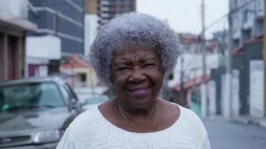 Şehir sokağında kameraya gülümseyen son sınıf siyahi bir kadın.