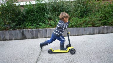 Little boy riding three wheeled scooter outdoors