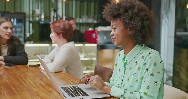 A happy black woman using laptop at coffee shop. One African American girl typing on computer keyboard smiling. A female entrepreneur person looking at laptop screen