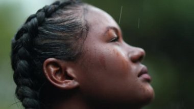 Yağmurda siyah bir kız. Yakın plan Afrikalı genç bir kadın yağmur yağarken gökyüzüne bakıyor.